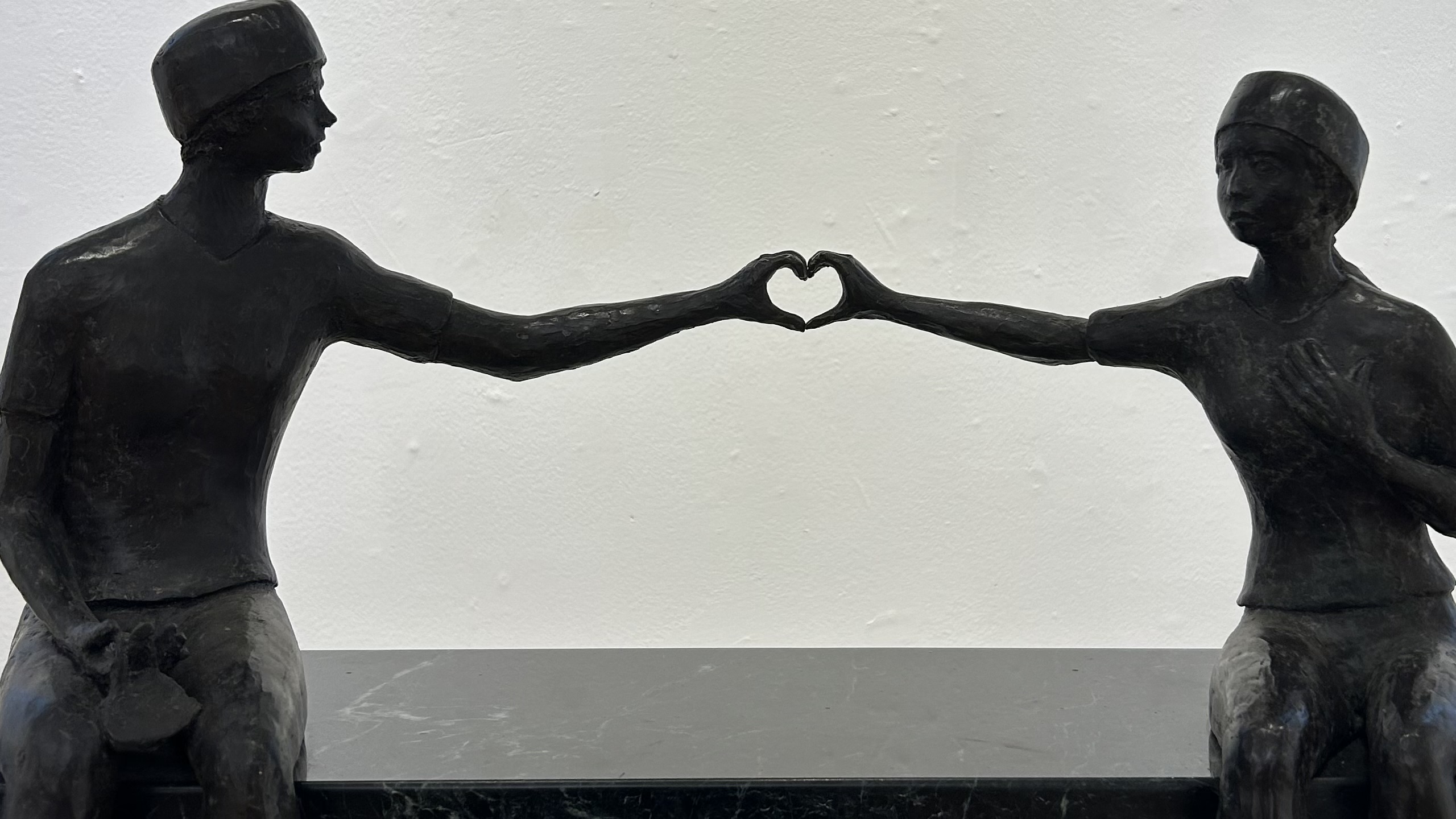 sculpture of two people making a heart sign w their hands