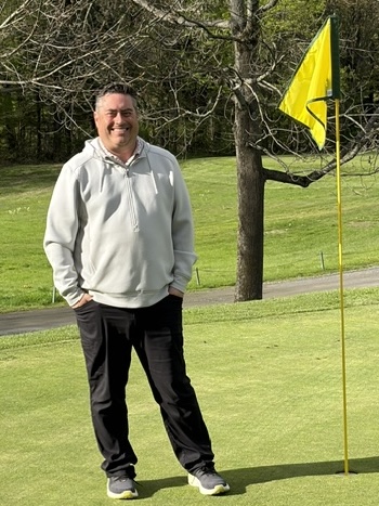 man standing on a golf greem beside a flag smiling