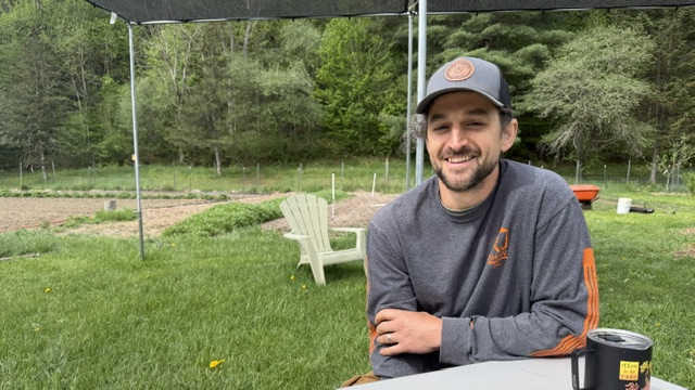 NAthan sitting at a table smiling with gardens bahind him