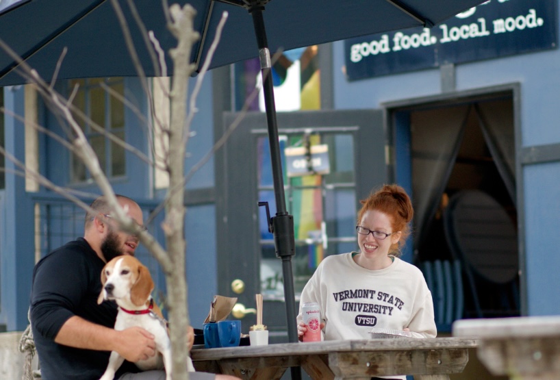 2 people eating outside, w a dog on a lap